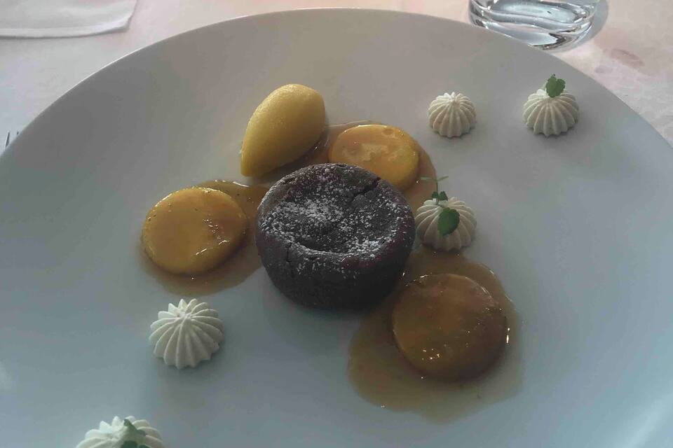 A dessert plate with a chocolate lava cake, caramelized bananas, and small white meringue-like balls.