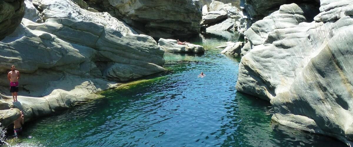 A rocky landscape with a clear water body and a person jumping off a rock.