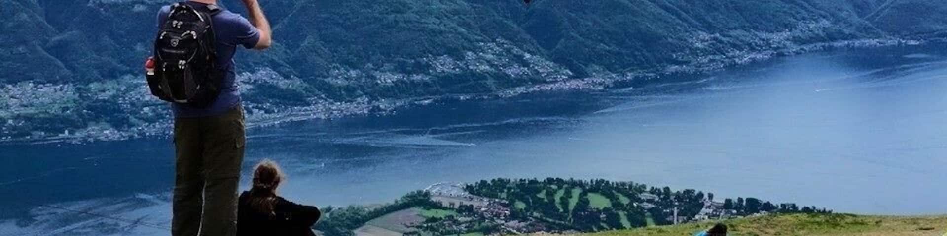 A person taking a photograph of a paraglider over a mountainous landscape with a lake below.