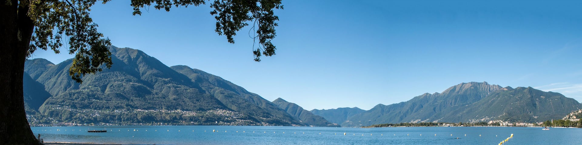 Lake Locarno - lake shore with pebble beach and high mountains of swiss alps in the background.