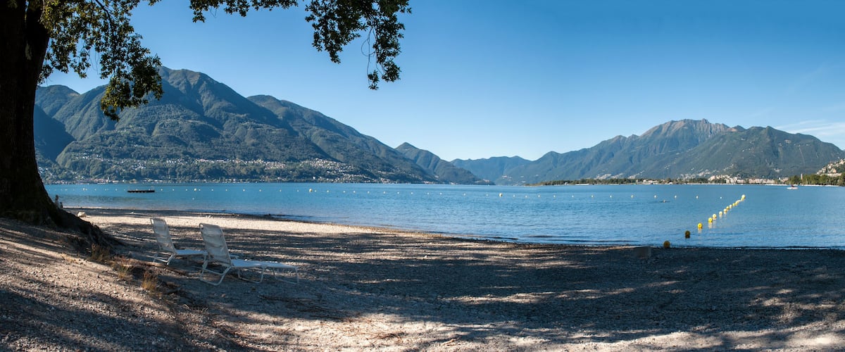 A beach with a mountain backdrop, a clear sky, and a few boats on the water.