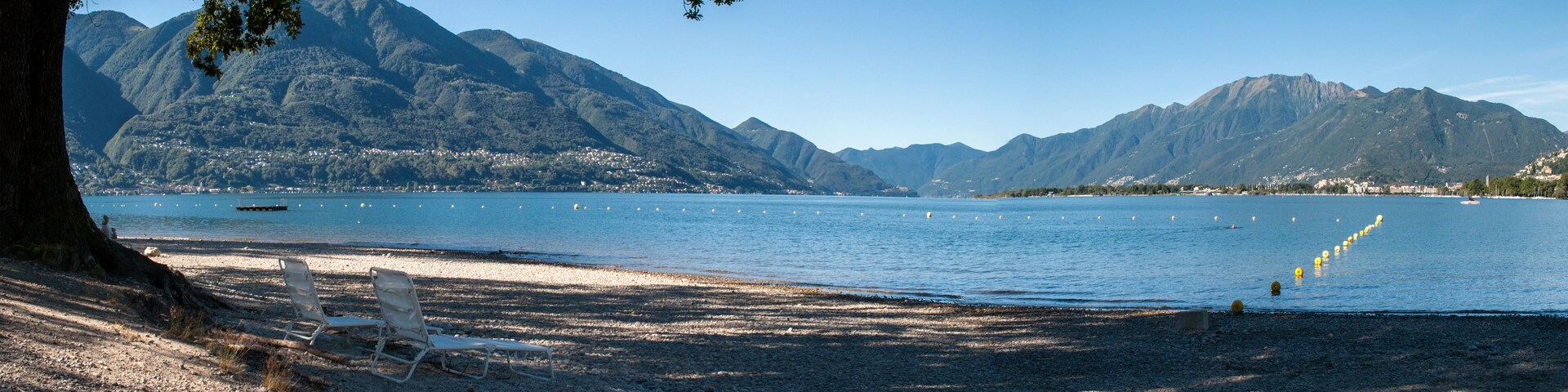 A beach with a mountain backdrop, a clear sky, and a few boats on the water.
