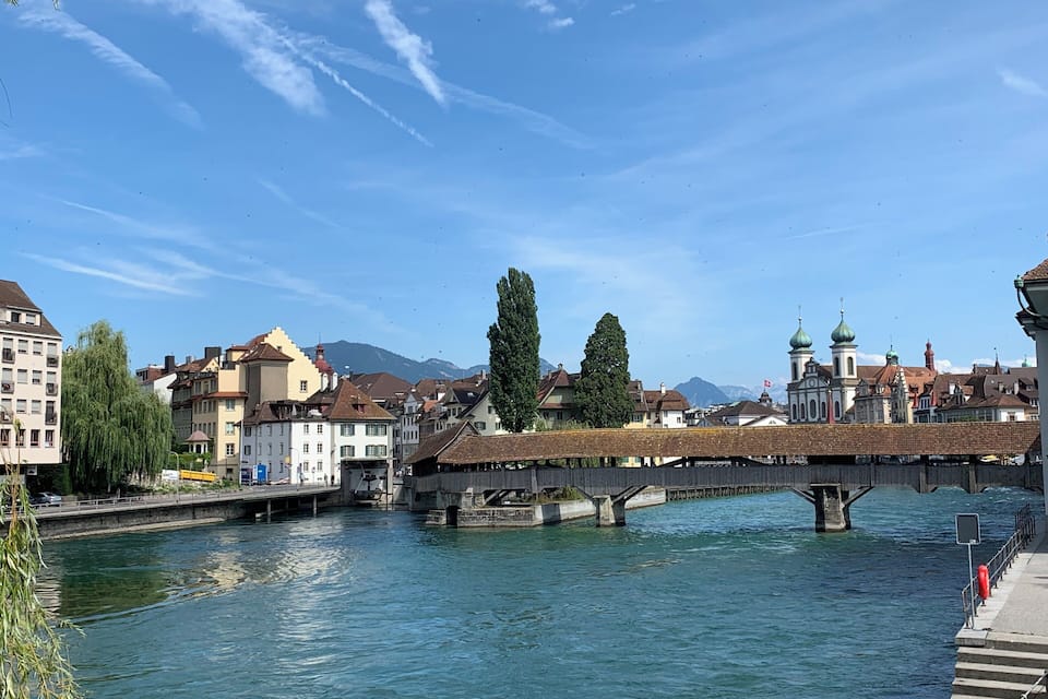 A river with a bridge, buildings, and mountains in the background.