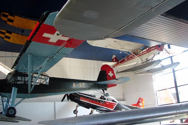 Une collection d’avions anciens, dont un appareil rouge et blanc portant le numéro d’immatriculation A-97, est exposée à l’intérieur.