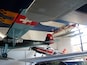 A collection of vintage aircraft, including a red and white plane with the registration A-97, displayed indoors.