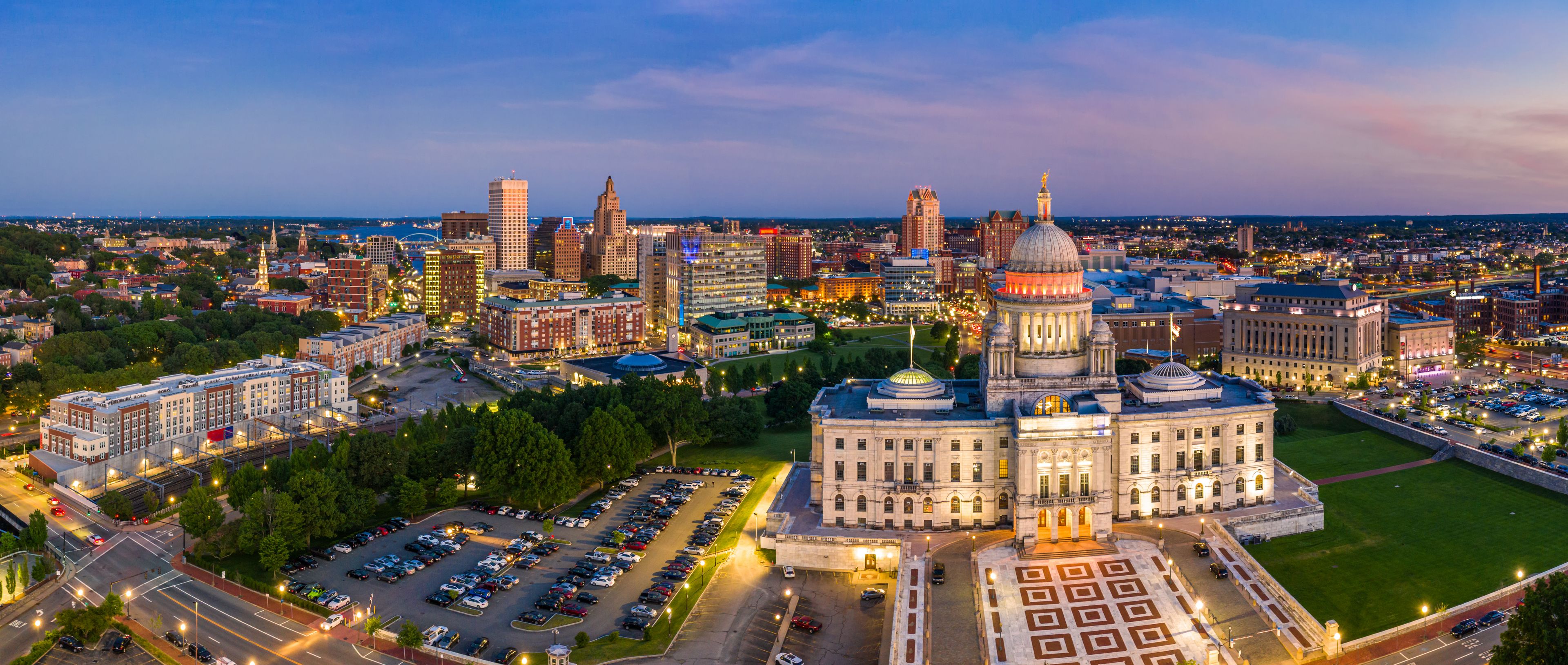 A cityscape at dusk with prominent buildings, including a large domed structure and a tall skyscraper.