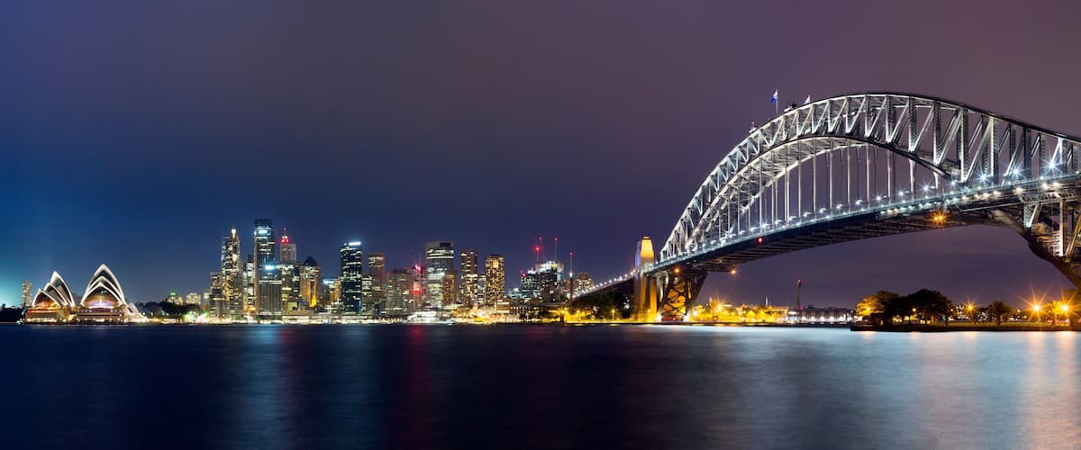 A nighttime cityscape with a prominent bridge and the Sydney Opera House.