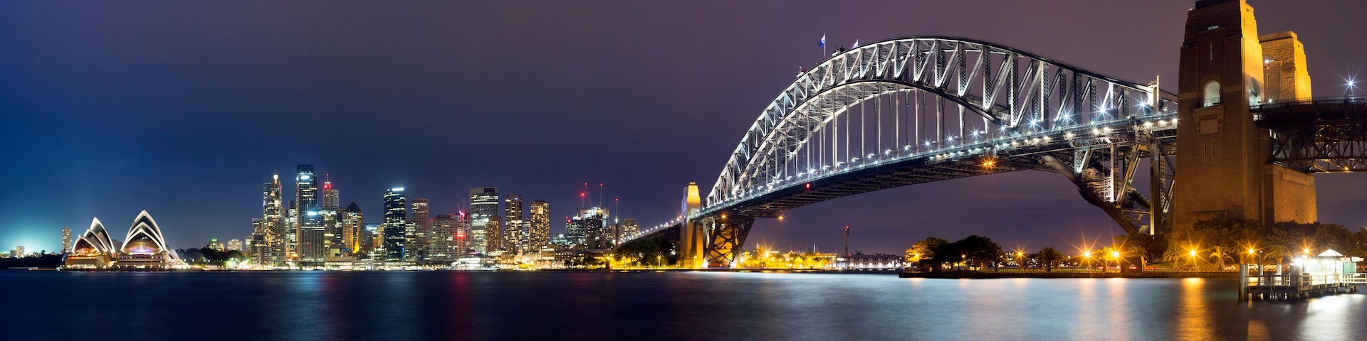 A nighttime cityscape with a prominent bridge and the Sydney Opera House.