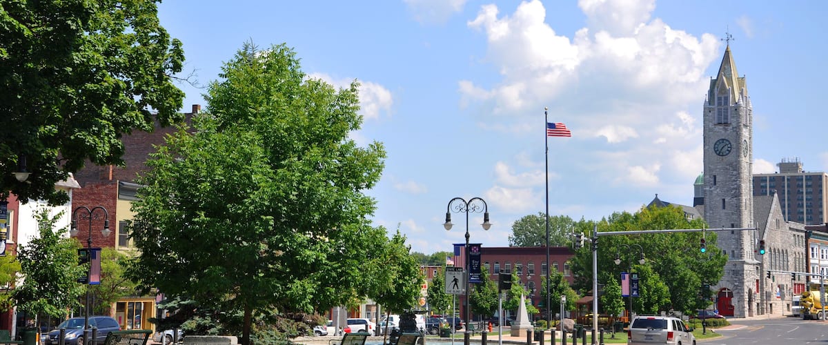 A street with a historic clock tower, a park with benches, and a clear blue sky.
