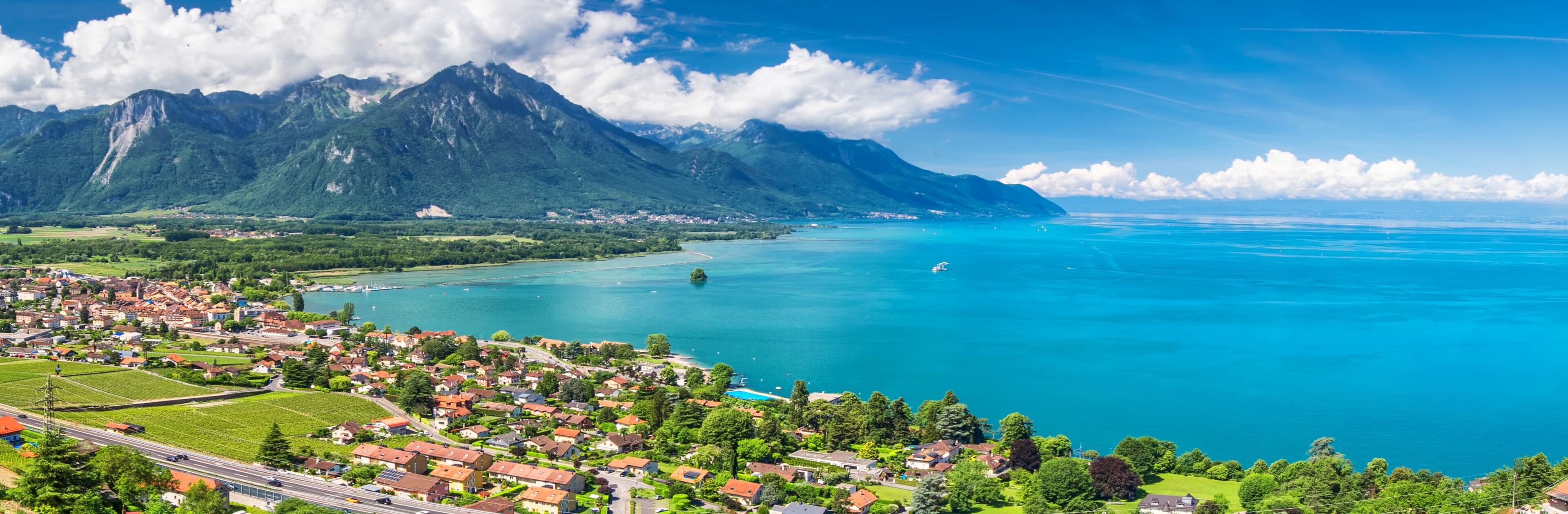 A coastal town with a mountain backdrop, clear blue waters, and lush greenery.