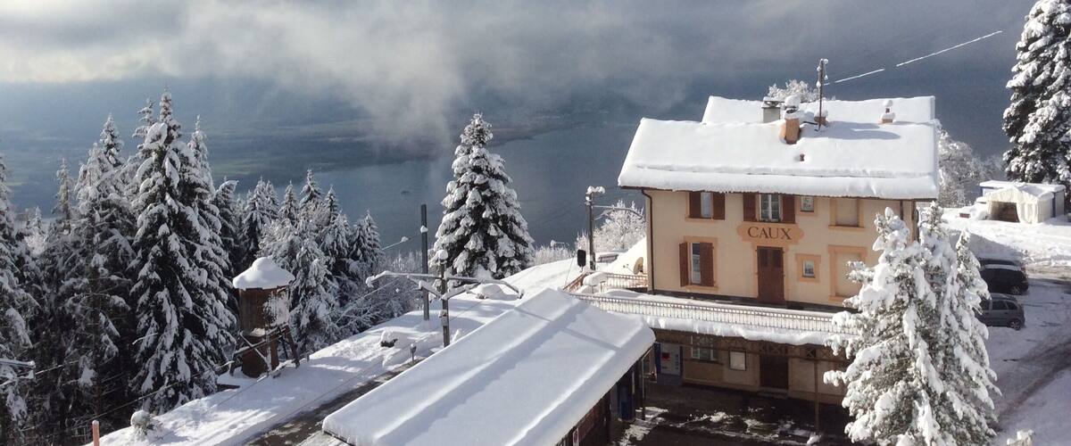 A snow-covered building with the sign "CAUX" in a mountainous area.