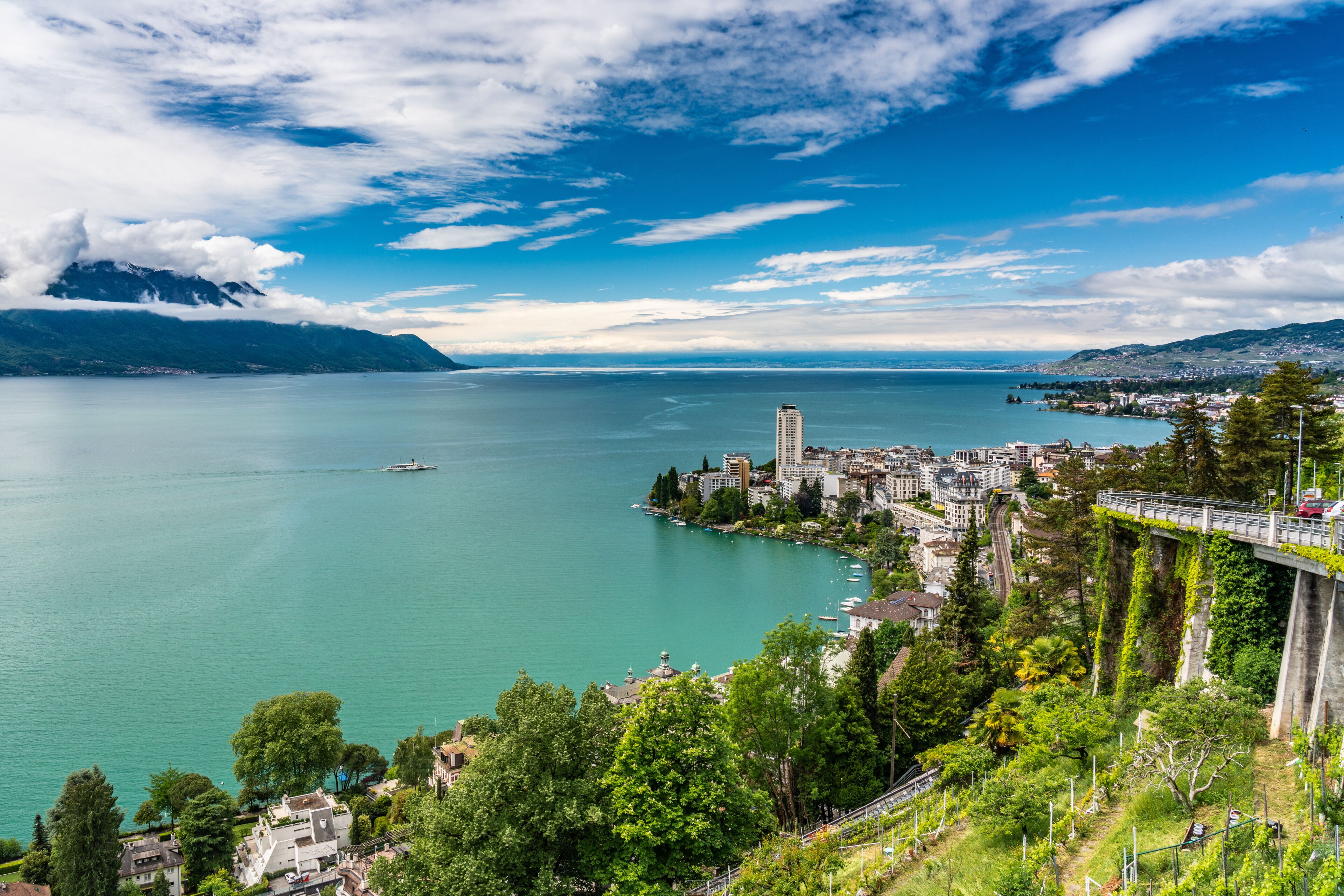 A lake with a bridge, a mountain in the background, and a cityscape along the shore.