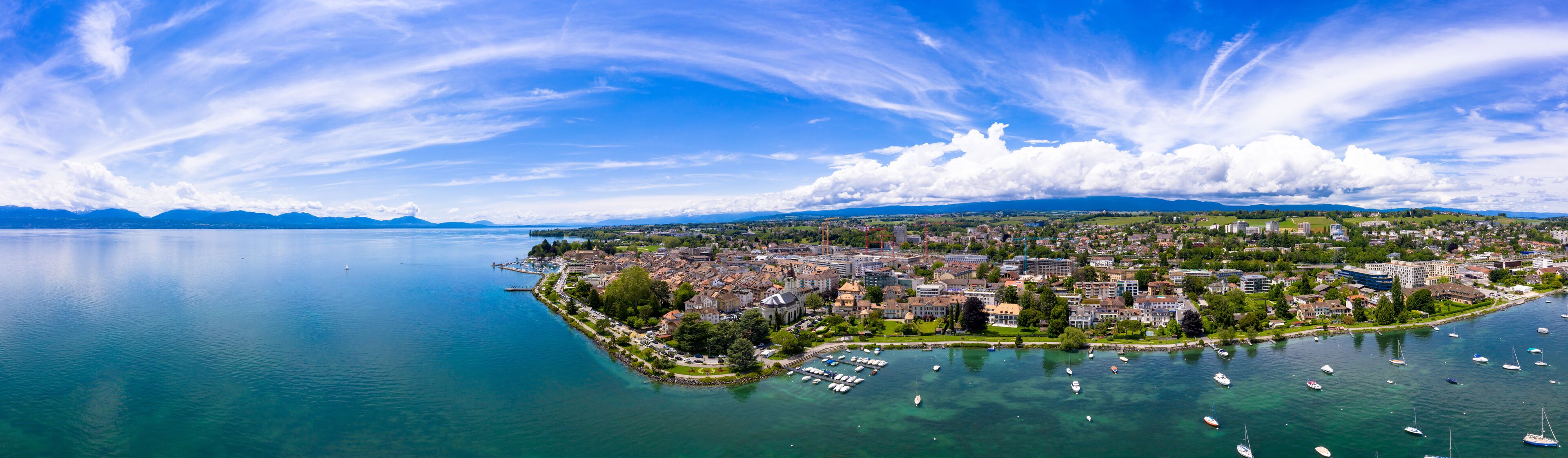 A coastal city with a marina, mountains in the background, and clear skies.