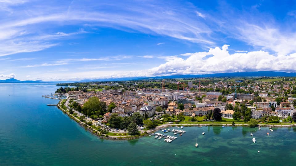 A coastal city with a marina, mountains in the background, and clear skies.