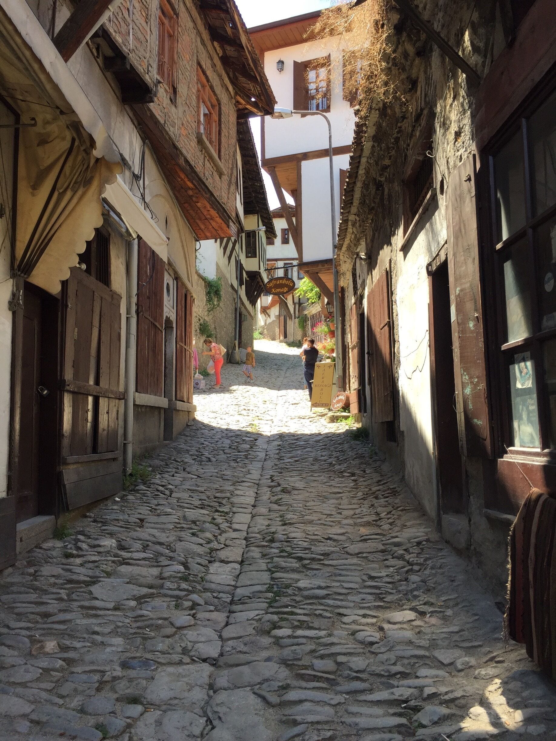 A cobblestone street in a historic town with traditional buildings and a sign for 'Sofranpolka Xonagi'.