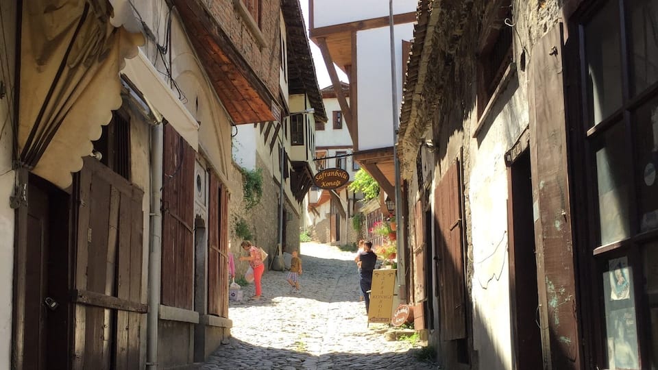 A cobblestone street in a historic town with traditional buildings and a sign for 'Sofranpolka Xonagi'.