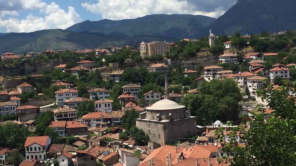 Uma cidade com edifícios de telhado vermelho, uma igreja com cúpula imponente e montanhas ao fundo.