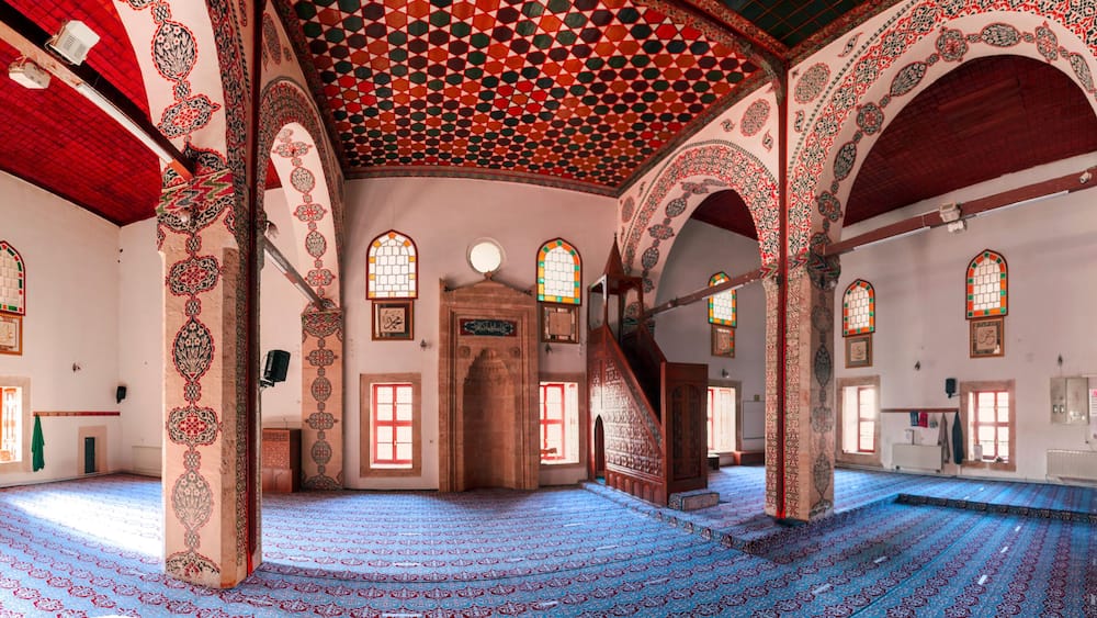 Un intérieur agrémenté d’arcs décoratifs, d’un tapis à motifs et de vitraux.