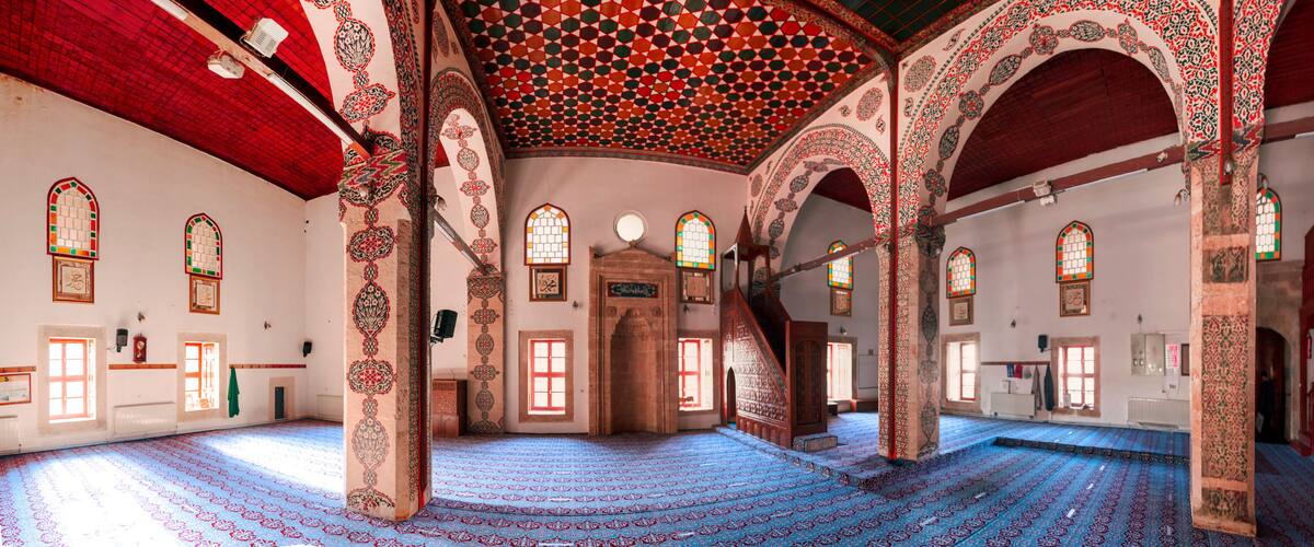 An interior with ornate arches, patterned carpet, and stained glass windows.