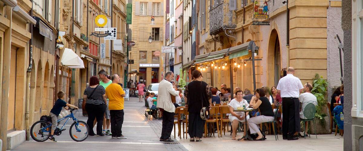 A bustling street with people dining at outdoor cafes, bicycles, and historic buildings with shutters.