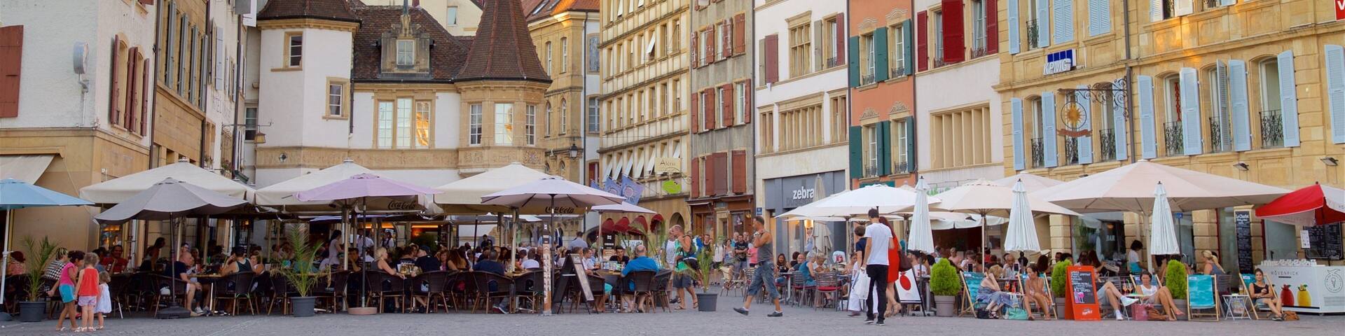 A bustling European square with historic buildings, outdoor cafes, and a prominent church spire.