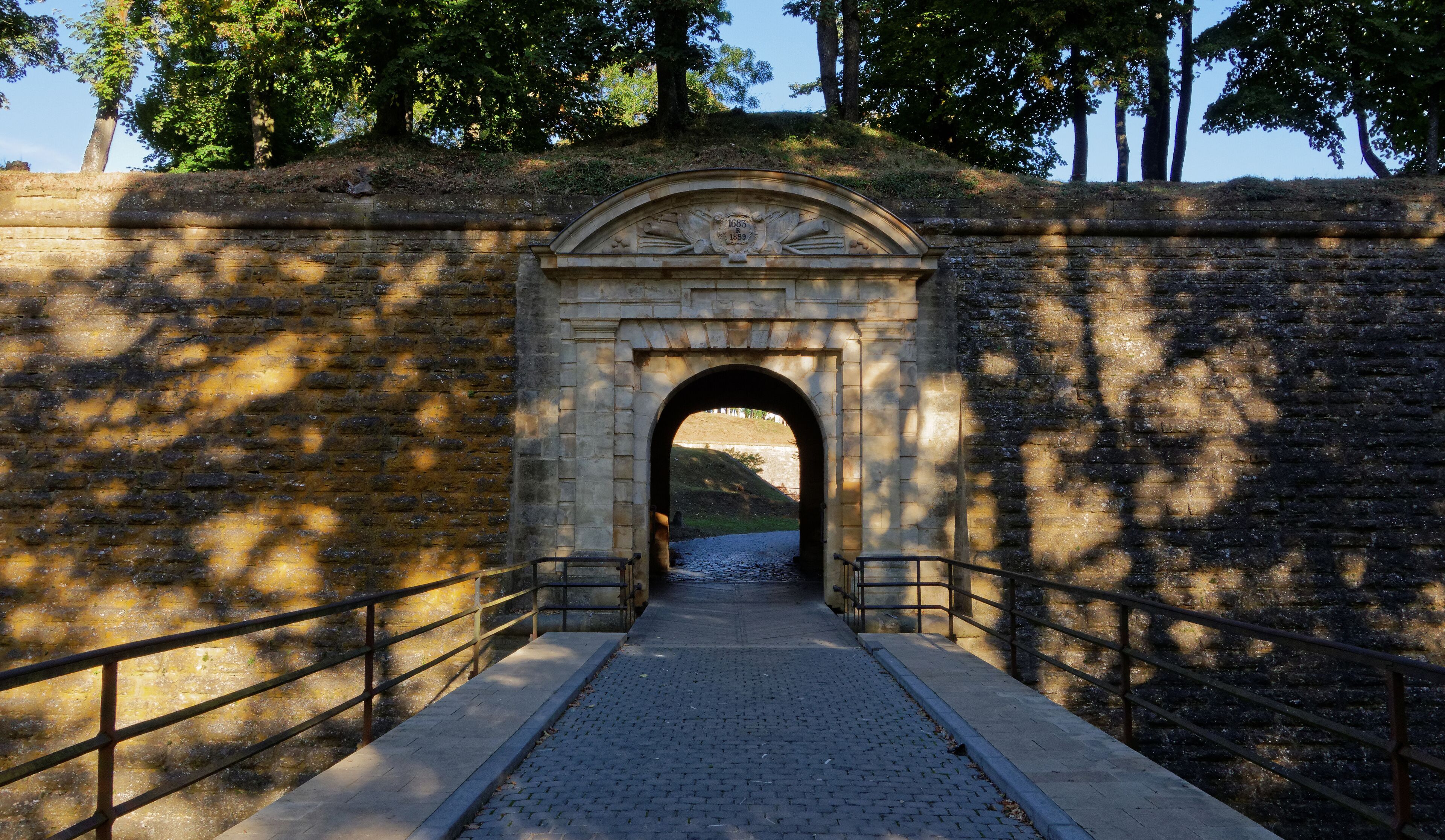 A stone bridge with an archway leading to a grassy area.