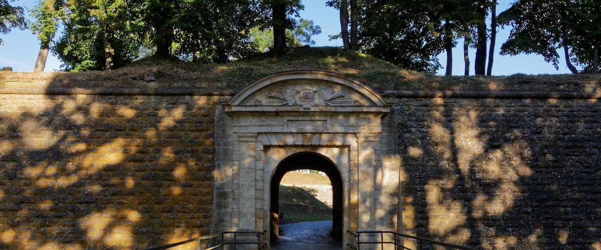 A stone bridge with an archway leading to a grassy area.