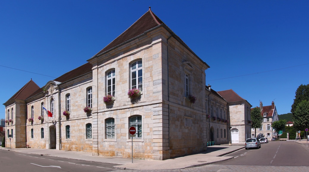 A historic stone building with arched windows and a red roof, situated on a sunny street.