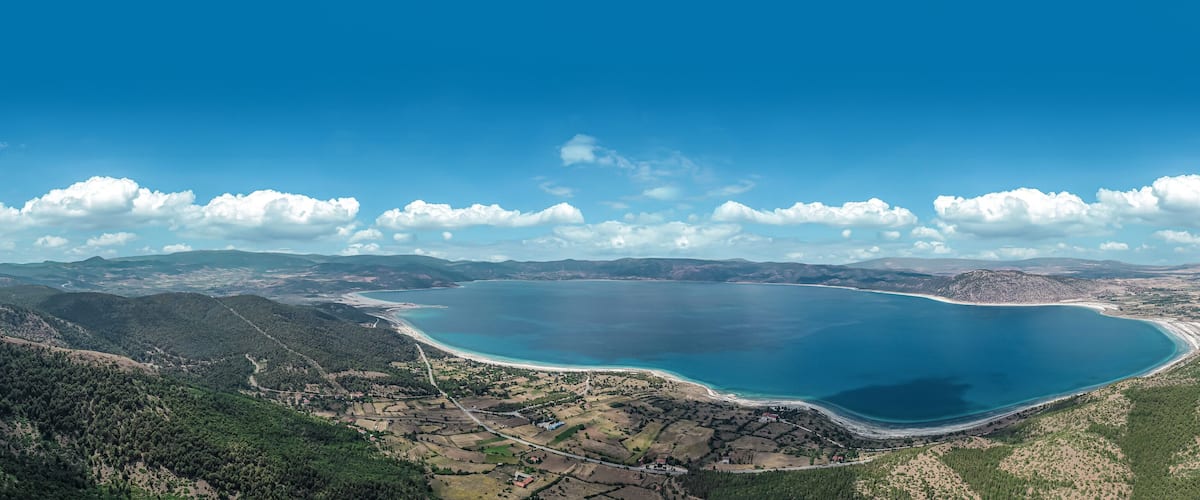 A coastal landscape with a large lake, surrounding hills, and a clear sky.