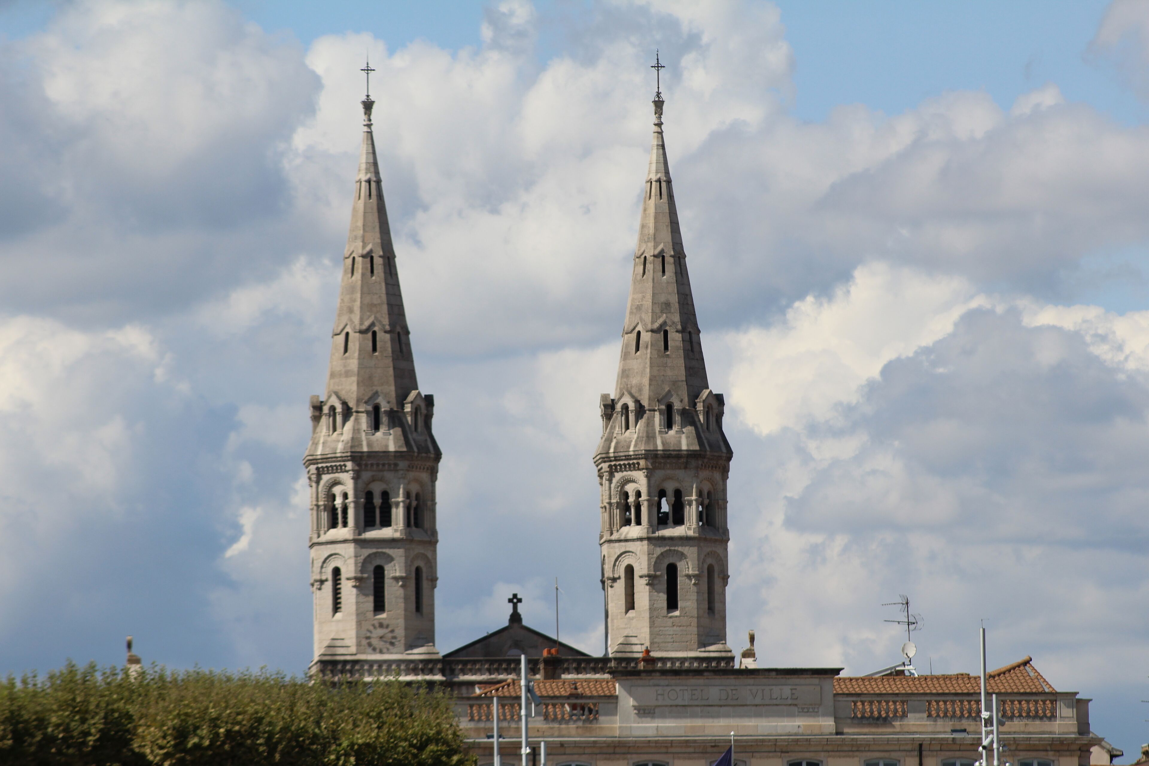 A historic building with two prominent towers and a cross at the top, under a partly cloudy sky.