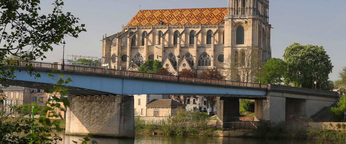 A cathedral with a patterned roof and a tall tower, under a bridge.