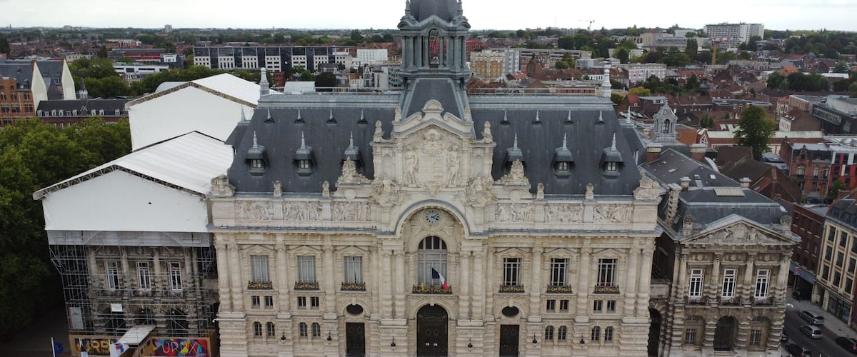 A historic building with ornate architecture, a clock tower, and a large open plaza with steps leading up to the entrance.