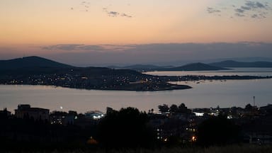 A coastal cityscape at dusk with a large body of water, a bridge, and distant mountains.
