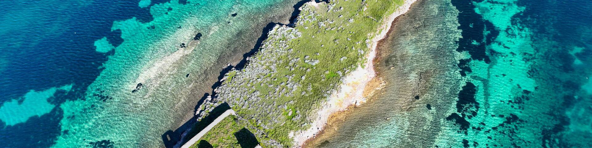 An aerial view of a small island with clear turquoise waters, a sandy beach, and a few structures.