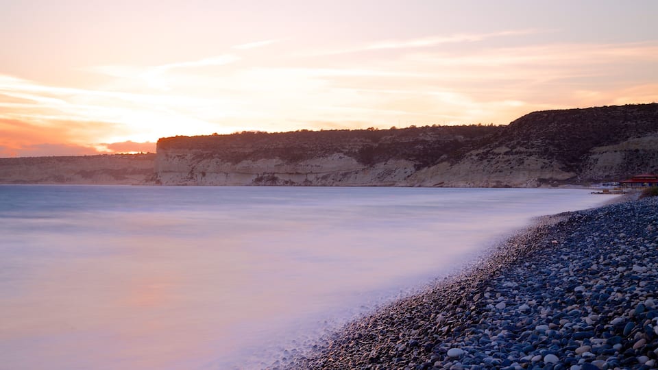 A pebbly beach with a rocky cliff and a sunset.