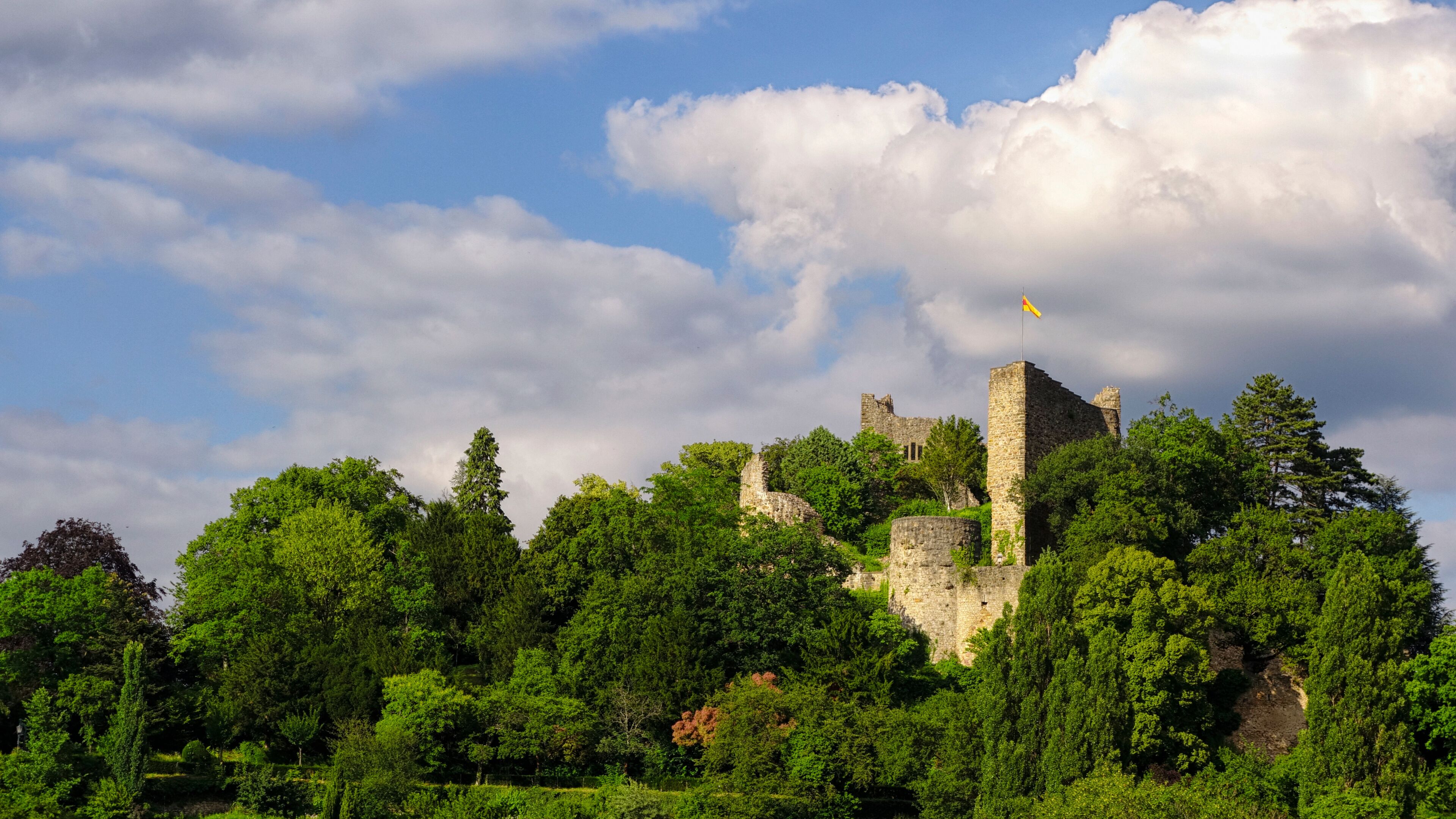 A historic castle surrounded by lush greenery and a partly cloudy sky.