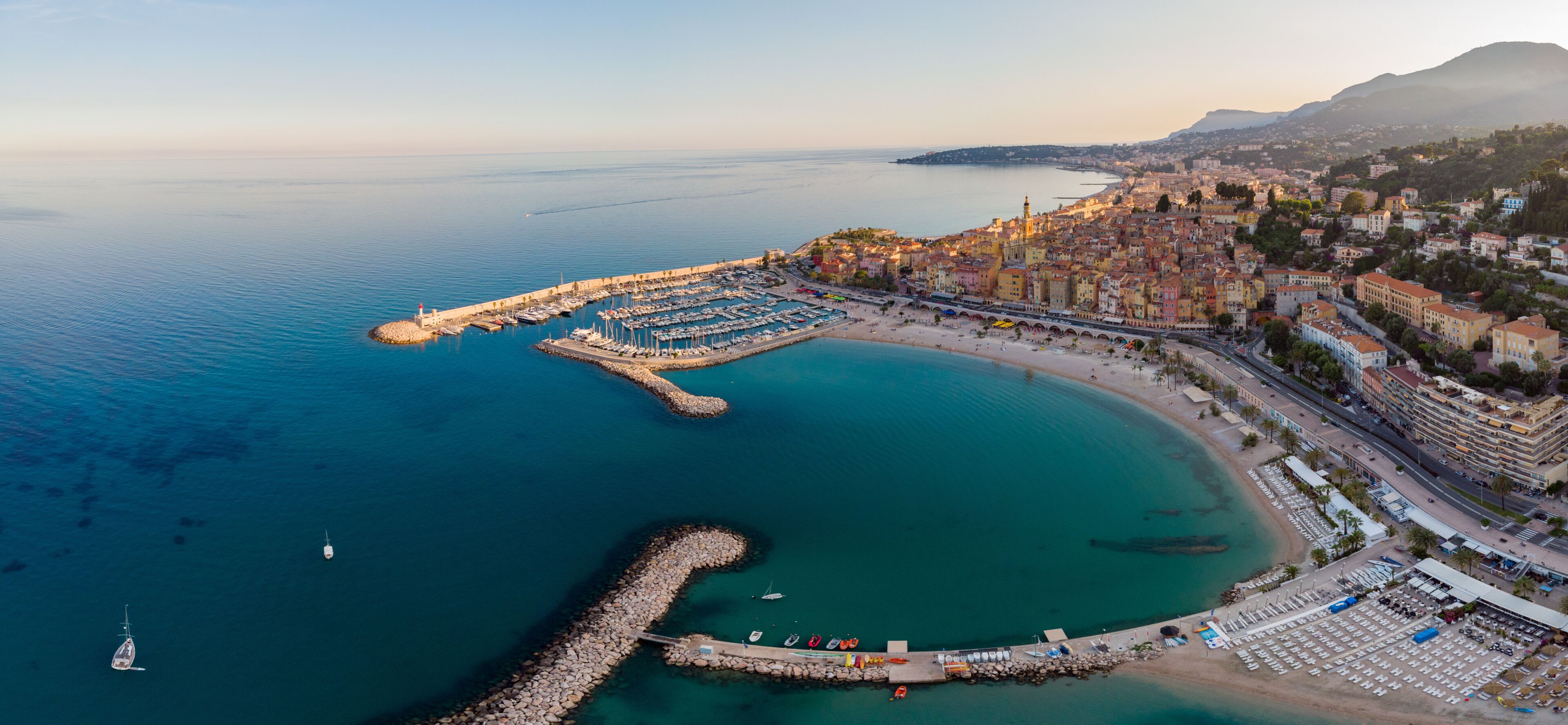 A coastal cityscape with a marina, a curved pier, and a densely built urban area.