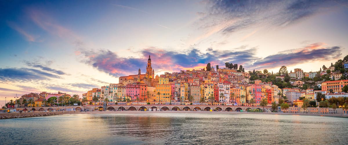 Un paysage urbain côtier avec des bâtiments aux couleurs vives, une tour imposante et un pont enjambant l’eau.