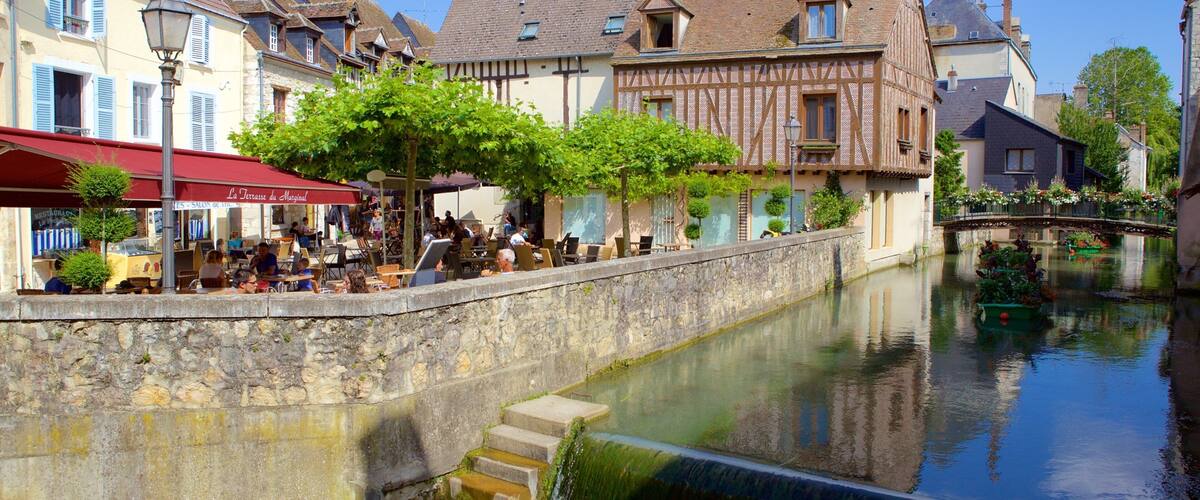 A riverside café with outdoor seating, historic buildings, and a bridge.