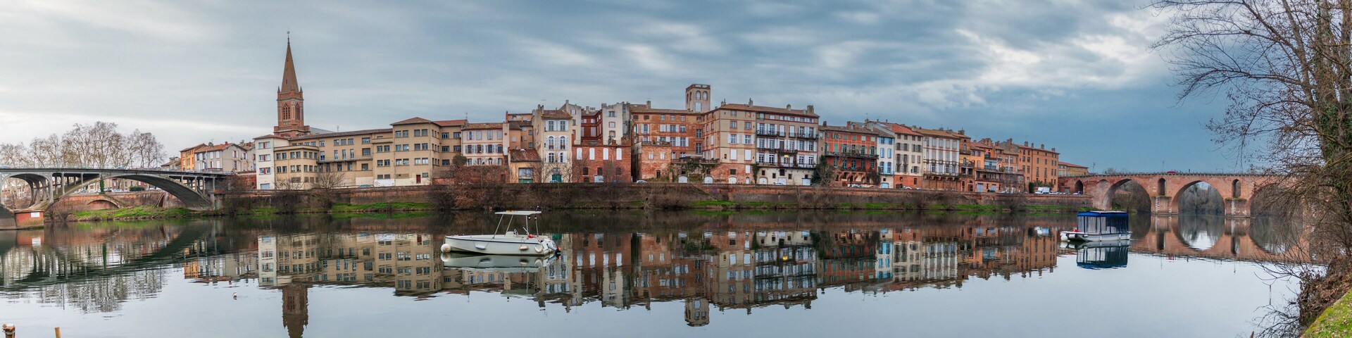 A river with a bridge, a tower, and colorful buildings reflecting in the water.