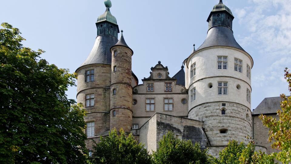 A historic castle with two prominent towers, a central courtyard, and surrounding trees.