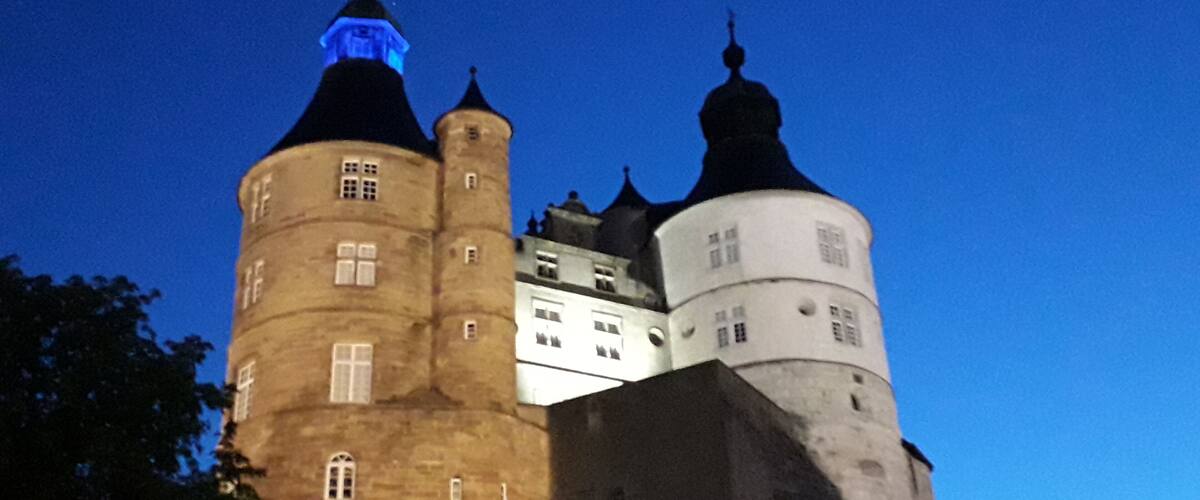A castle with multiple towers and a lit spire against a twilight sky.