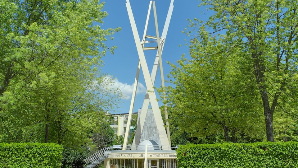 A modern sculpture with intersecting white beams in a park.