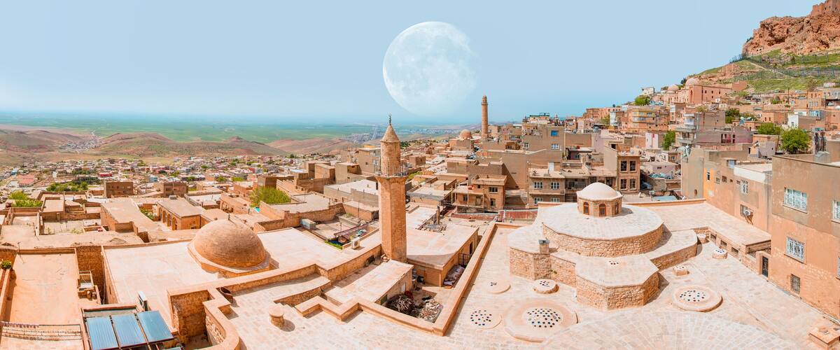 A cityscape with a prominent mosque, a large dome, and a mountain in the background.