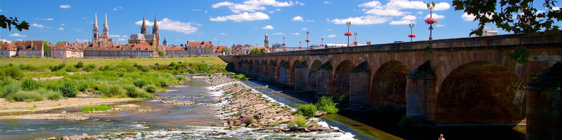 Un río fluye bajo un puente de piedra, con un paisaje urbano al fondo.