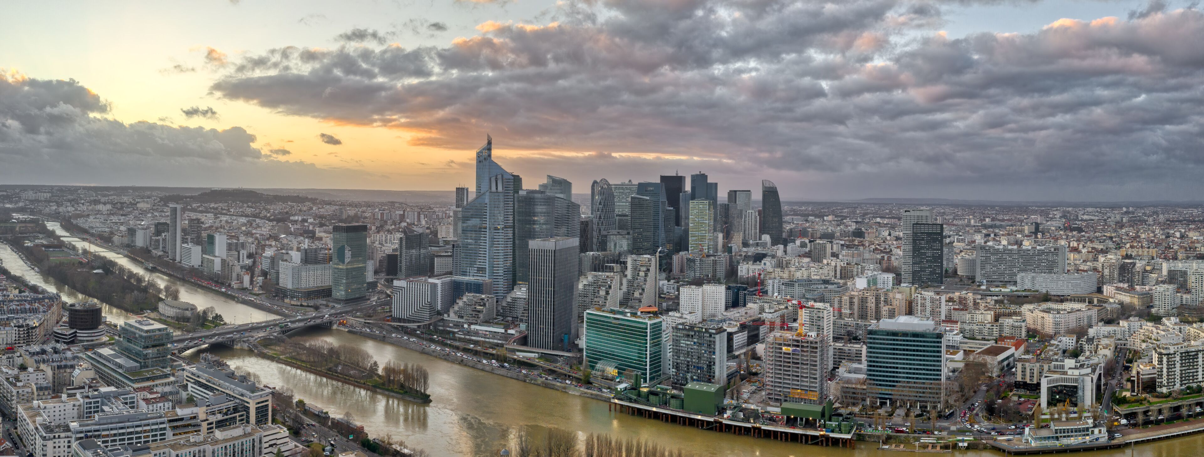 A cityscape with a river, modern skyscrapers, and a cloudy sky.