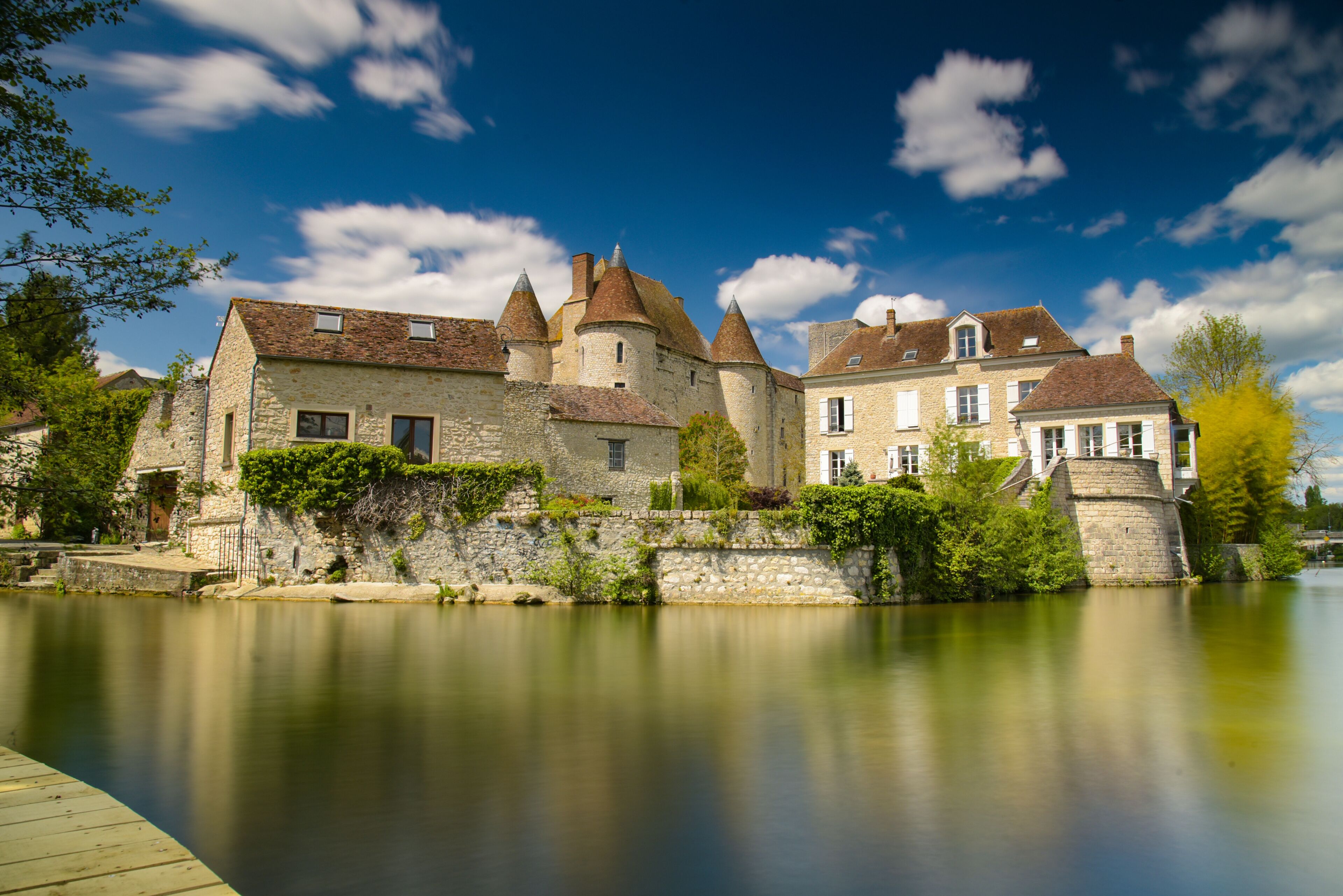 A historic stone castle by a calm river with a wooden dock.
