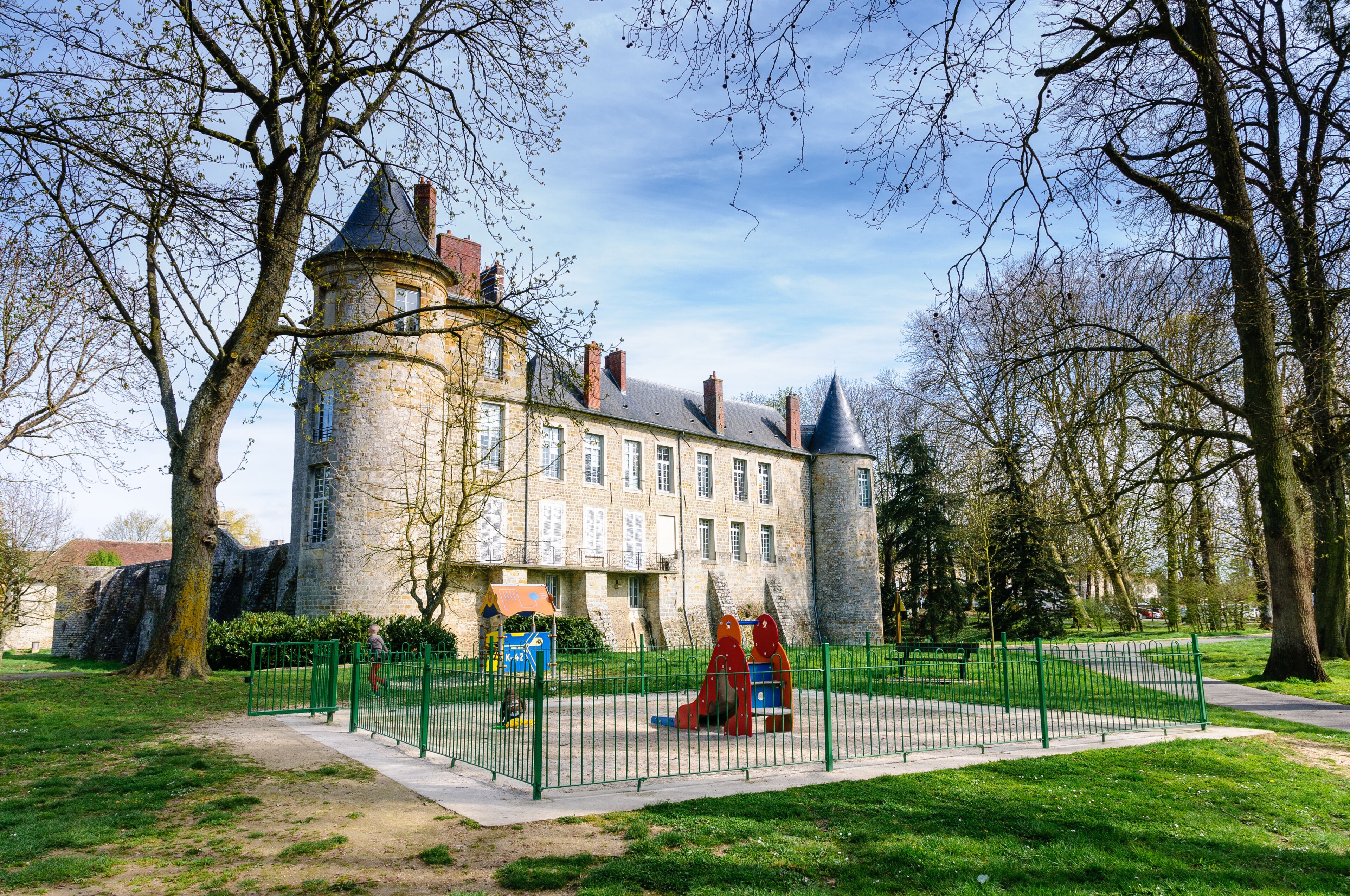 A castle-like building with a tower, surrounded by a green park and trees.