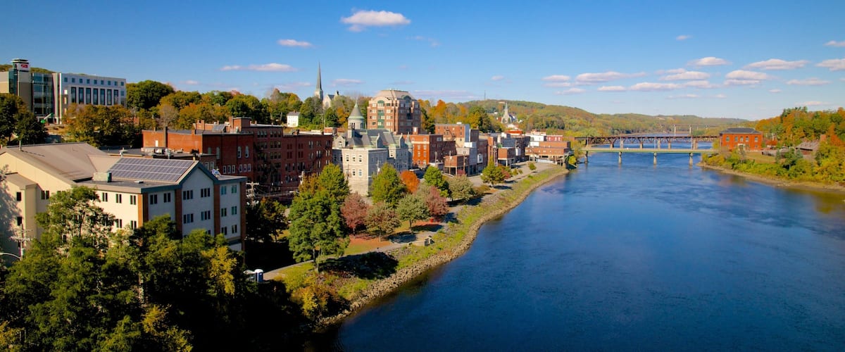 A riverside town with historic buildings, a prominent church steeple, and a bridge over the river.
