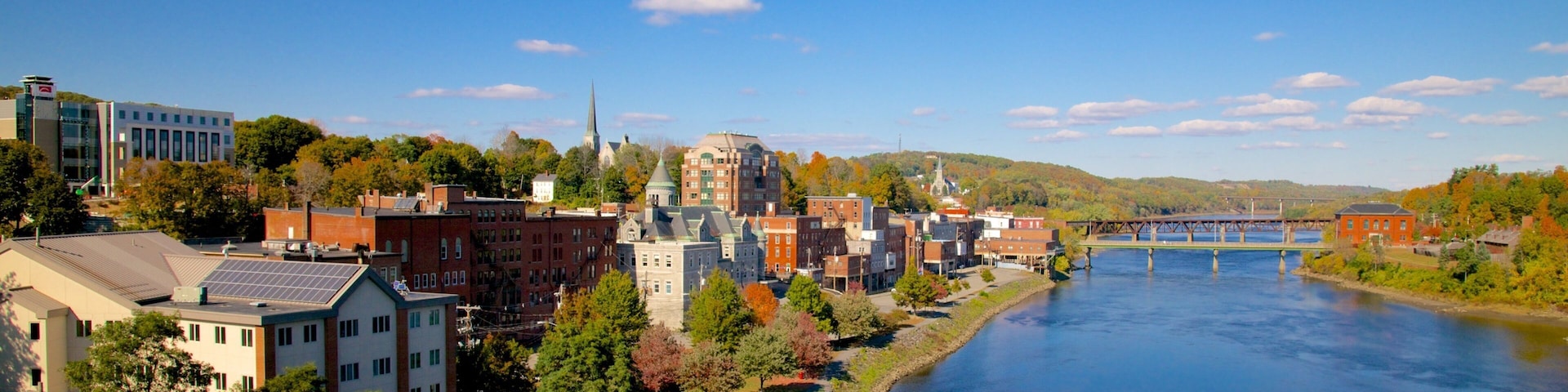 A riverside town with historic buildings, a prominent church steeple, and a bridge over the river.
